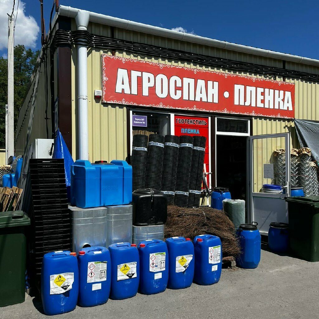 Фасад магазина АгроХозСнаб: вывеска, бочки и рулоны у входа